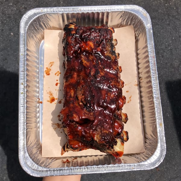 A rack of glistening BBQ ribs in a foil pan with parchment paper, ready to serve.