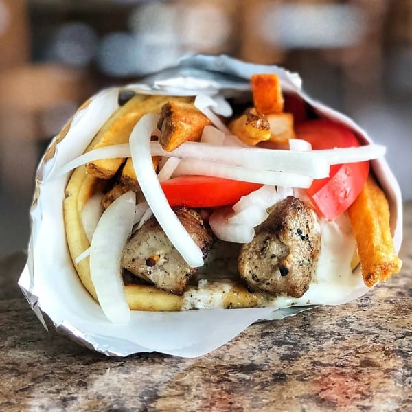 A gyro with meat, onions, tomatoes, fries, and sauce, wrapped in foil on a speckled counter.