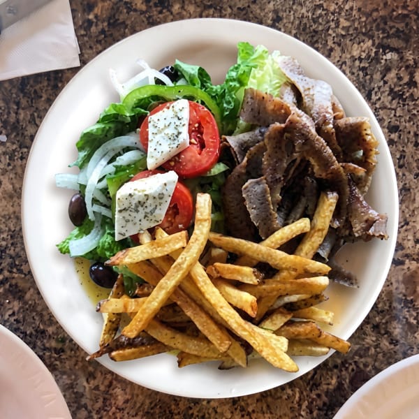 A plate of gyro meat, french fries, and a Greek salad with feta, tomatoes, and olives.