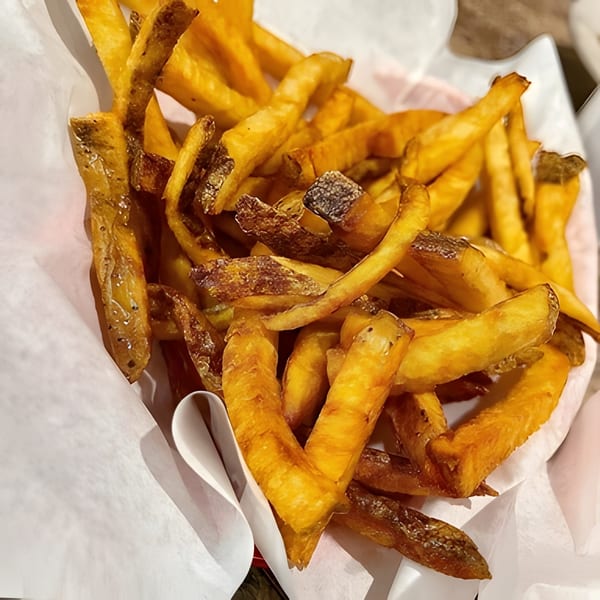 Close-up of a basket of golden-brown, skin-on french fries served in white paper.