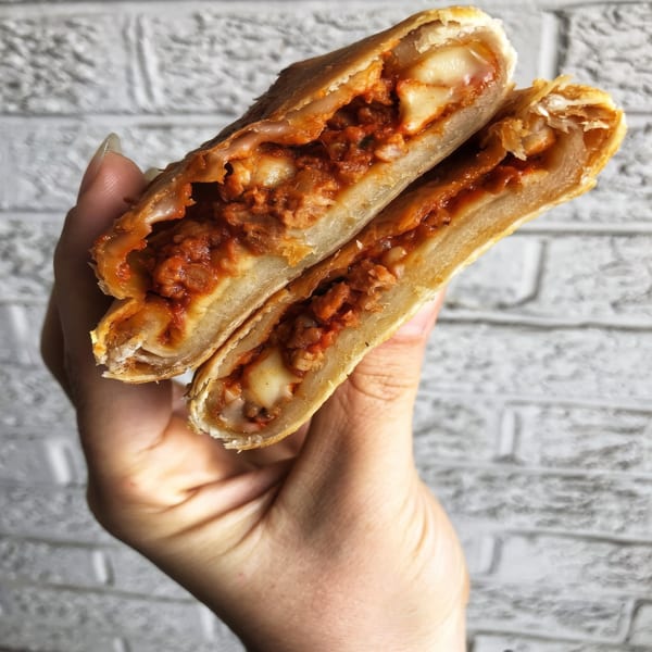 A hand holds a golden-brown calzone, cut in half, revealing a rich red filling with melted cheese.