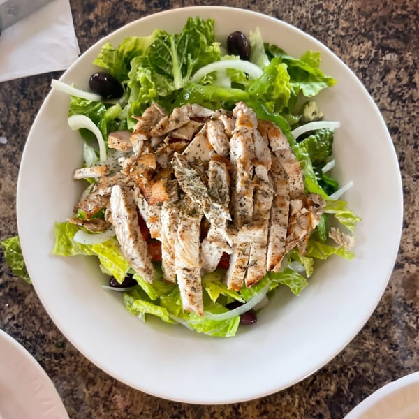 Grilled chicken salad with romaine lettuce, onions, and black olives in a white bowl.