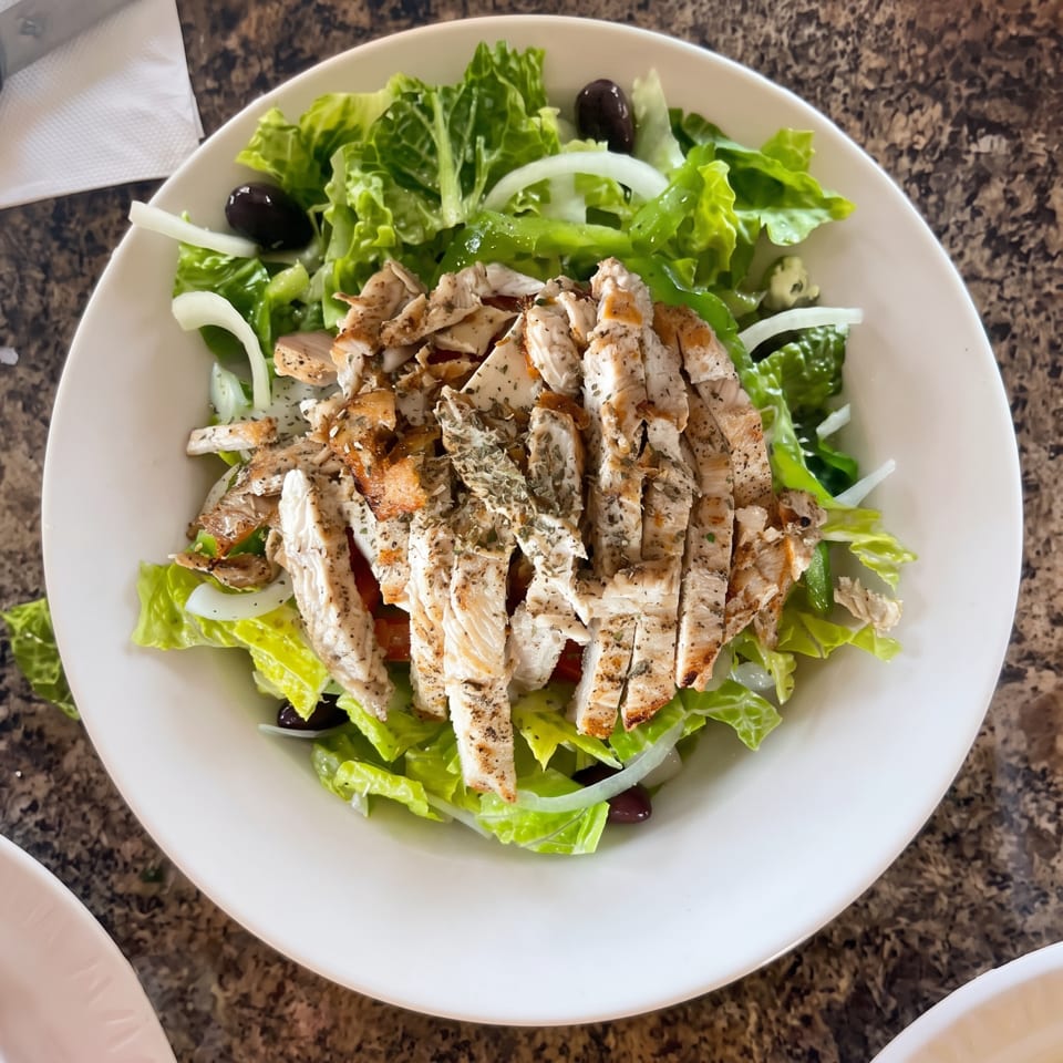 Grilled chicken salad with romaine lettuce, onions, and black olives in a white bowl.